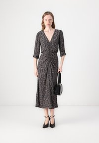 Maxikleid mit tiefem V-Ausschnitt, dreiviertel Ärmeln und gerafftem Vorderteil in einem mehrfarbigen Muster. Kombiniert mit schwarzen Plateauschuhen und einer Handtasche.
