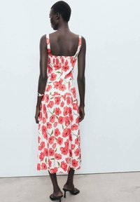 Floral midi dress in white, featuring red and green poppy prints. Spaghetti straps, back smocking detail, and flowy fabric. Heeled sandals.