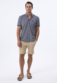 Grå polo shirt med korte ærmer, knap-lukning foran og kontrastfarvet krave, parret med lyse beige shorts og brune sandaler.
