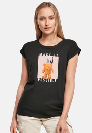 Schwarzes T-Shirt mit kurzen Ärmeln, das ein grafisches Design eines Teddybären und den Text "MACH ES MÖGLICH" auf einem hellrosa Hintergrund zeigt.