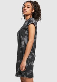 Naisel krussis hobusesabas, kes kannab musta ja halli triibulist lühikeste varrukatega kleiti, seisab profiilis tavalise tausta ees.