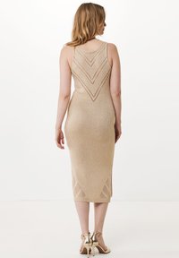 Dzianinowa midi sukienka w metalicznym złocie, z okrągłym dekoltem, wzorami w zygzak oraz bocznymi rozcięciami. W połączeniu ze złotymi sandałami na wysokim obcasie.