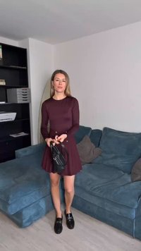 Μαρέν μακρυμάνικο φόρεμα με φαρδύ φουστάνι, συνδυασμένο με μαύρες τζιν μποτες. Το μοντέλο κρατά μία μικρή μαύρη τσάντα. Υφασμάτινος μπλε καναπές στο φόντο.