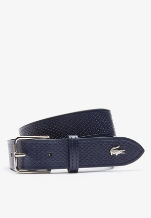 Marineblauwe gestructureerde leren riem met zilveren metalen gesp en klein zilveren krokodillenlogo aan het uiteinde, opgerold op een witte achtergrond.