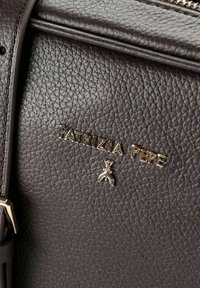 Bolso de cuero marrón oscuro con superficie texturizada, logo "PATRIZIA PEPE" en tono dorado y un pequeño adorno decorativo.