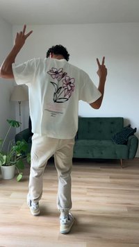 T-shirt branca com um design floral em roxo e preto nas costas, emparelhada com calças de jogging em tom creme e ténis multicoloridos.