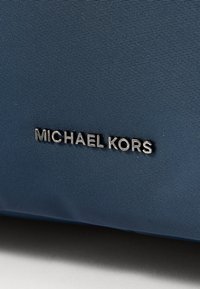 Niebieska teksturowana tkanina z metalowymi literami "MICHAEL KORS" przymocowanymi na stałe.