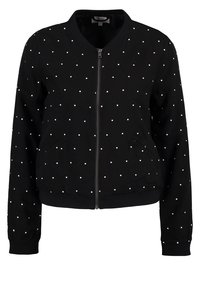 Giubbotto bomber nero con zip frontale, caratterizzato da pois bianchi, polsini e vita a coste. Due tasche laterali. Tessuto di superficie liscia.