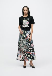 Zwart T-shirt met kleurrijk grafisch ontwerp, gecombineerd met een lange, patroonrijke rok met abstracte tijger- en stermotieven. Zwarte hakken.