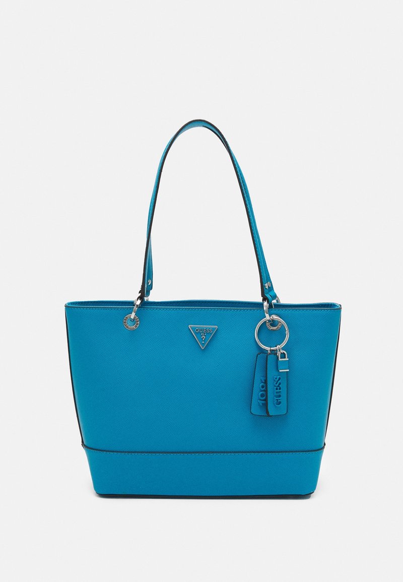 Sac tote bleu Guess avec double poignée, accessoires argentés, logo triangulaire et deux étiquettes de marque suspendues sur un fond clair.
