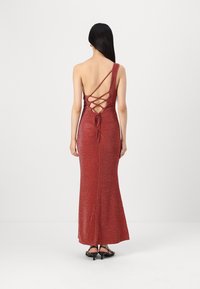 Robe de soirée rouge, scintillante, à une épaule avec un détail lacé dans le dos et une silhouette fluide, touchant le sol.
