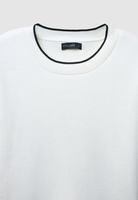Maglione bianco con texture e colletto a coste nero. L'etichetta mostra "CALLIOPE" e la taglia "S". Design semplice, senza ulteriori motivi o dettagli.