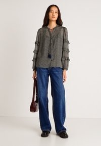 Γκρίζα μπλούζα με υφή, διαφανή μανίκια με ρίγες και κορδόνια. Συνδυασμένη με φαρδιές μπλε τζιν παντελόνες και μια μικρή μπορντό τσάντα.