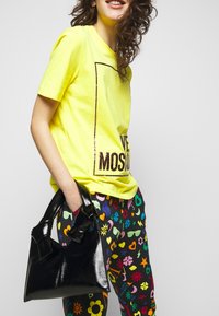 Neonowo żółta koszulka z napisem "LOVE MOSCOW", do tego kolorowe, wzorzyste spodnie z motywem serc i kwiatów; w ręku błyszcząca czarna torebka.