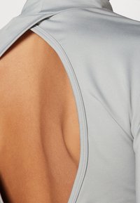 Indumento grigio chiaro con un ampio taglio sulla schiena, caratterizzato da tessuto liscio e design aderente. I bordi sono accuratamente rifiniti con cuciture per un aspetto pulito.