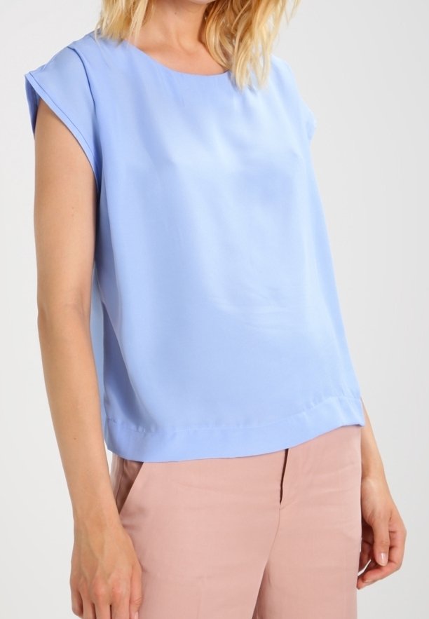 Krátký rukáv, světle modrá blůza vyrobená z hladkého materiálu. Má kulatý výstřih a rovný lem, v kombinaci s růžovými kalhotami.