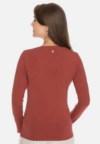 Langsleeve shirt in roestkleur, gemaakt van zachte stof. Heeft een ronde halslijn en een kleine metalen accent aan de achterkant.