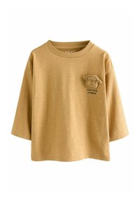 T-shirt à manches longues de couleur jaune moutarde, texture douce, coupe décontractée, avec une appliqué de mouton et le texte "AMUSER AVEC DES AMIS" sur la poitrine gauche.
