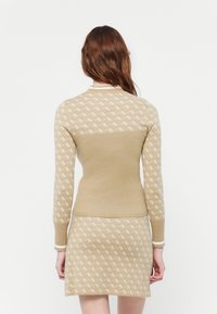 Abito in maglia beige con maniche lunghe, caratterizzato da un motivo a diamante in bianco sporco. Collo e polsini a coste con strisce bianche. Texture morbida.