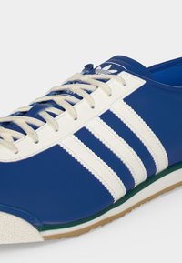 Μπλε αθλητικό παπούτσι Adidas με άσπρες τρεις ρίγες, άσπρα κορδόνια και λαστιχένια σόλα, με το λογότυπο στη γλώσσα και λεπτομερείς ραφές.