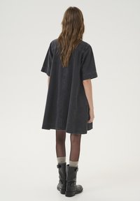 Svart denimbalklänning med korta ärmar, lös passform och sidofickor, tillsammans med svarta stövlar med spännen och grå strumpor.