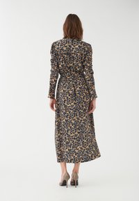 Blommönstrad klänning med lång ärm i beige med marinblå blommor, med åtstramad midja och full kjol. Bärs med ljusa högklackade skor.