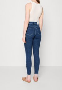 Tmavě modré skinny džíny s vysokým pasem, dvěma zadními kapsami a štíhlým střihem. Kombinované s světlým topem a plochými sandály.