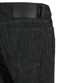 Mustat denim-farkut, joissa on nahkapatche vyötäröllä, pieni takatasku ja hillitty tekstuuripinta.