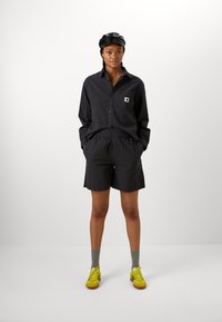 Zwart geruit kortmouwshirt met een patch zak, gecombineerd met bijpassende shorts. Gedragen met grijze sokken en gele sneakers.