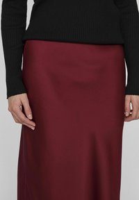 Jupe en satin bordeaux au toucher lisse, associée à un haut noir à côtes ajusté. Mettez l'accent sur la silhouette élégante et le contraste riche des couleurs.