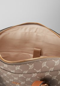Beige mønstrede håndtaske med åben guldlukning, der viser en glat lyserød stofindvendig og en lille inderlomme.