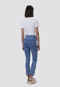 Jeans de mezclilla azul con cintura alta, piernas estrechas y detalles de botones en el tobillo, combinados con una camiseta blanca básica.