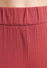 Gros plan sur la taille d'une personne portant un pantalon rouge à taille haute côtelé avec une ceinture élastique.