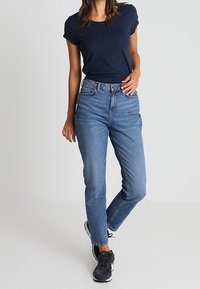 Granatowy t-shirt z okrągłym dekoltem w zestawieniu z jasnoniebieskimi dżinsami z wysokim stanem. Sneakersy mają czarno-biały kolor.