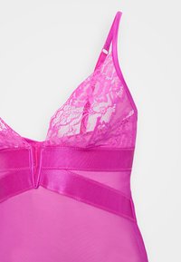 Bralette en dentelle rose avec un sous-vêtement transparent, comprenant des bretelles réglables, une bande en satin lisse et des détails en dentelle florale sur les bonnets.