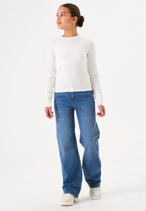 Weißes, geripptes Langarmshirt kombiniert mit lockeren blauen Jeans und weißen Sneakers. Das Outfit ist lässig und auf Komfort ausgelegt.