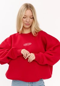 Czerwona bluza z nadmiernie dużymi rękawami, szczegóły ściągaczy, biała wyszywana logo i luźny, skrócony krój. Miękka bawełniana tkanina.