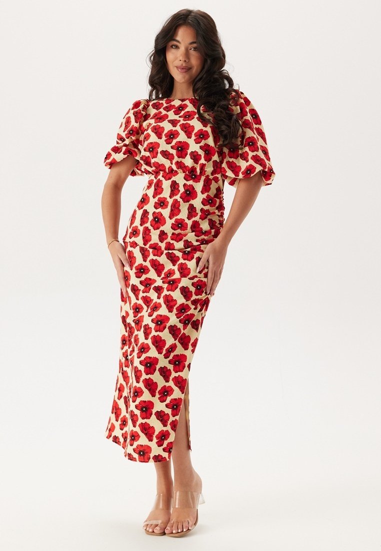 Robe à imprimé floral rouge avec manches bouffantes, silhouette ajustée et fente sur le côté. Fabriquée en tissu léger, avec un fond crème.