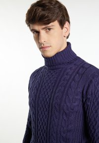 Maglione a collo alto lavorato a maglia in viola, caratterizzato da un motivo testurizzato e un colletto a coste. Il materiale sembra morbido e spesso.