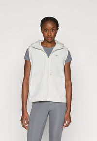 Ελαφρύ, αμάνικο γιλέκο σε ανοιχτό γκρι ύφασμα με κλείσιμο με φερμουάρ και ρυθμιζόμενο κουκούλα. Διαθέτει ομαλή υφή και λογότυπο ως διακοσμητικό στοιχείο.