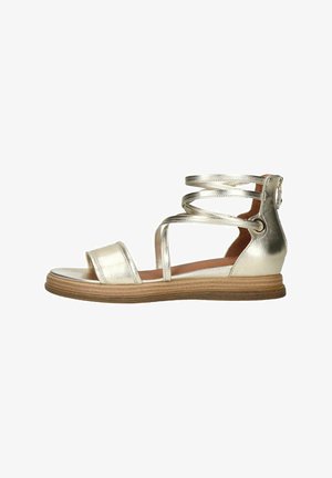 Metallic gold sandal with flat sole, open toe, and crisscross ankle straps. Features a wooden-textured midsole and circular accent on the heel.