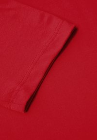 Roter Stoff mit glatter Textur, der einen Nahaufnahmem der Ärmelnaht zeigt. Die Nähte sind sichtbar, was auf eine hochwertige Verarbeitung hinweist.