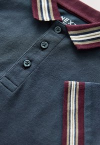 Dunkelblaues Polohemd mit einem kastanienbraunen Kragen, der gestreifte Akzente in Beige und Creme aufweist. Enthält drei schwarze Knöpfe und eine Brusttasche.