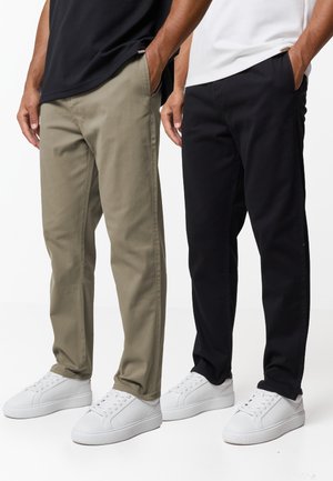 Due uomini in piedi uno accanto all'altro, che indossano pantaloni casual a gamba dritta, uno in verde oliva e l'altro in nero, abbinati a sneaker bianche.
