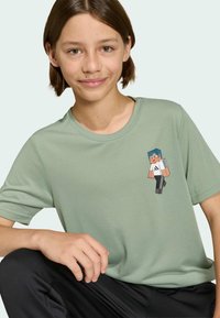 Svetlozelené bavlnené tričko s krátkym rukávom, na ktorom je na hrudi potlačená postava z Minecraftu. Postava má modré vlasy a neformálny outfit.