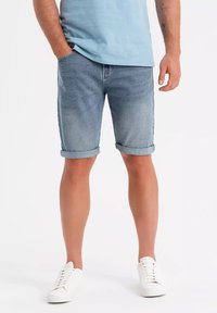 Pantalones cortos de mezclilla en azul claro, con un corte clásico y dobladillos doblados. Combinados con zapatillas blancas, mostrando un estilo casual y veraniego.
