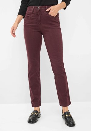 Burgunderfarbene Baumwollhosen mit tailliertem Schnitt, Fünf-Taschen-Stil und Knopfverschluss. Kombiniert mit schwarzen Slippern mit goldenen Beschlägen.