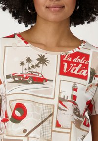 Haut à manches courtes avec un imprimé graphique à thème plage en rouge, beige et blanc, représentant des voitures, des palmiers et des phares.