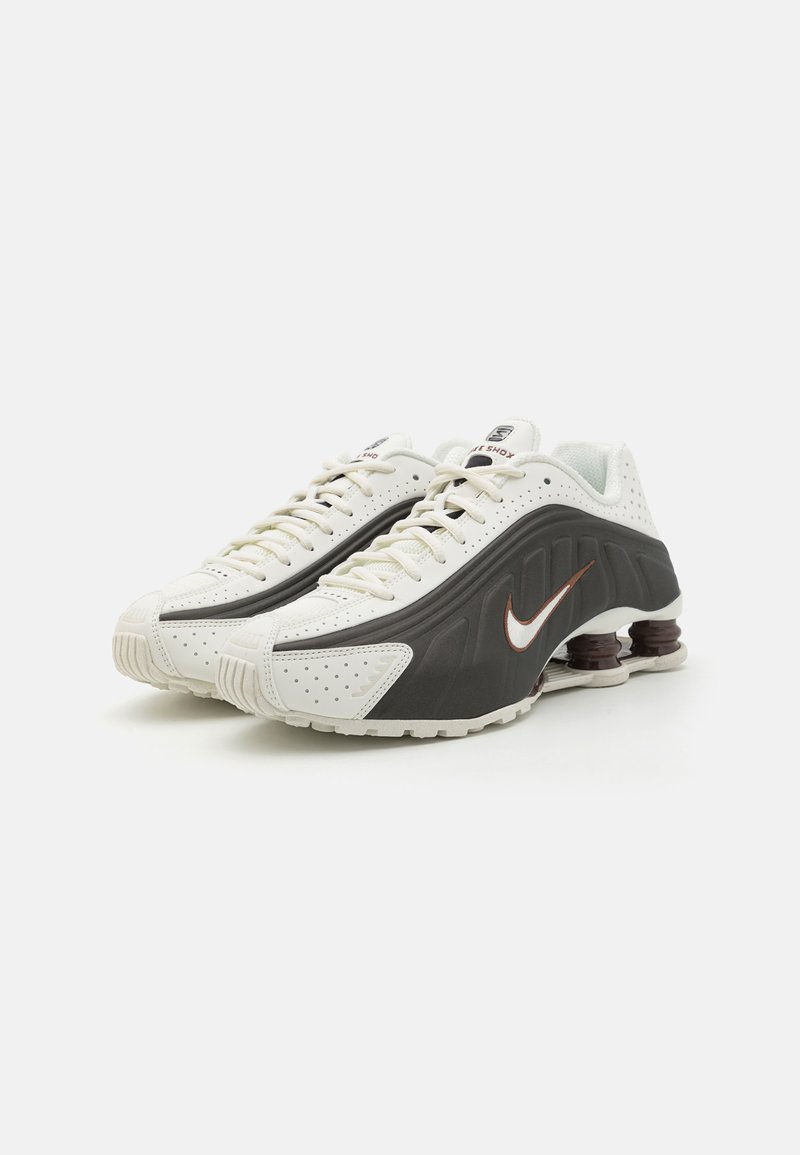 Nike-Sneaker mit weißem und dunkelgrauem Textil, perforierten Details, einem markanten, geschwungenen Design und braunen Gummipufferelementen.