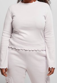 Ljusrosa ribbad långärmad topp med en volang i halsringningen och nederdelen, med åtsittande ärmar och en något kortad design.